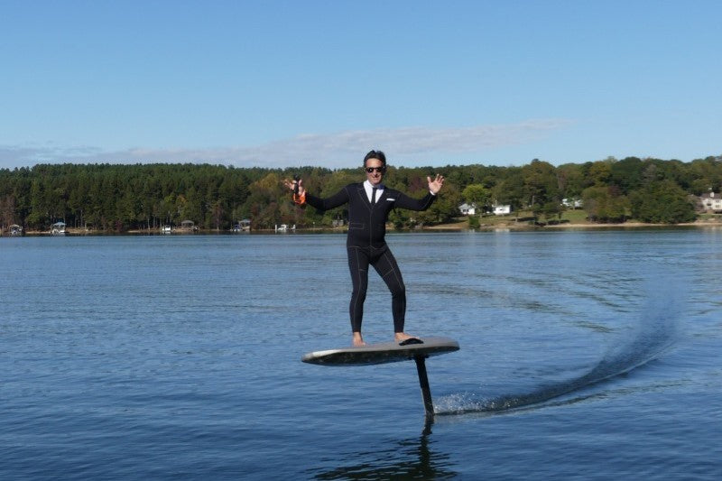 Man gekleed in een net pak en zonnebril op aan het eFoilen op het water