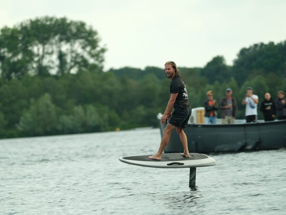 Man aan het eFoilen met toeschouwers in een boot op de achtergrond