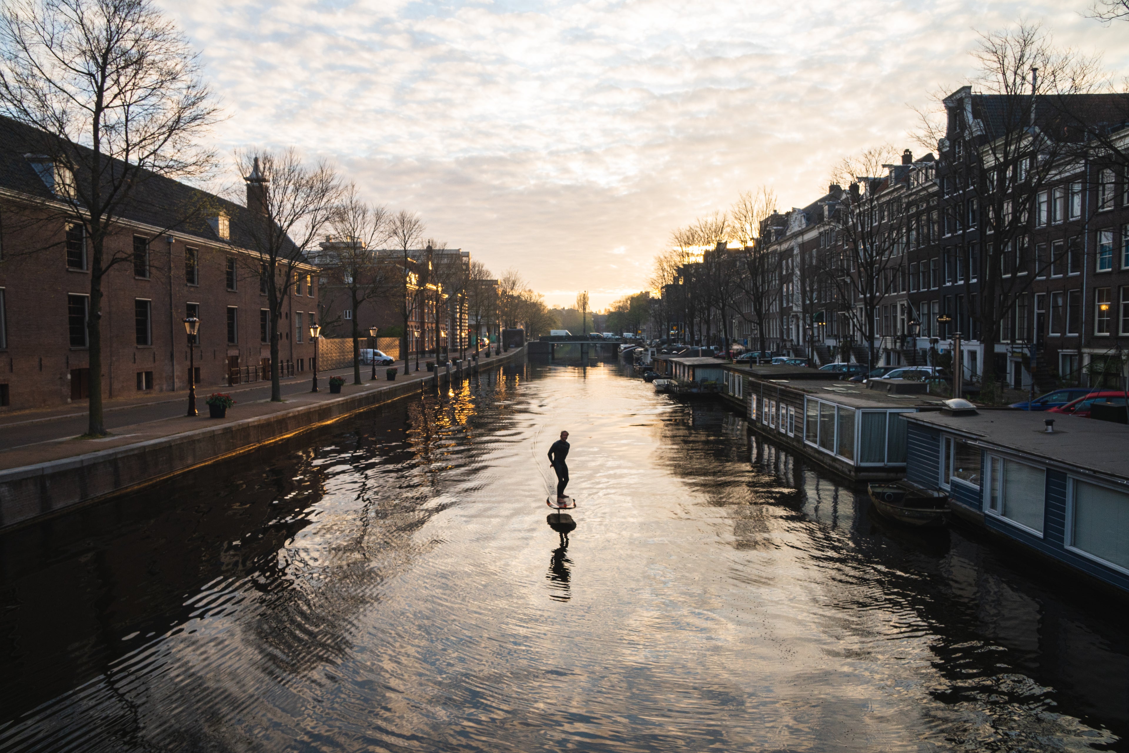 Man aan het eFoilen in de grachten van Amsterdam tijdens zonsondergang