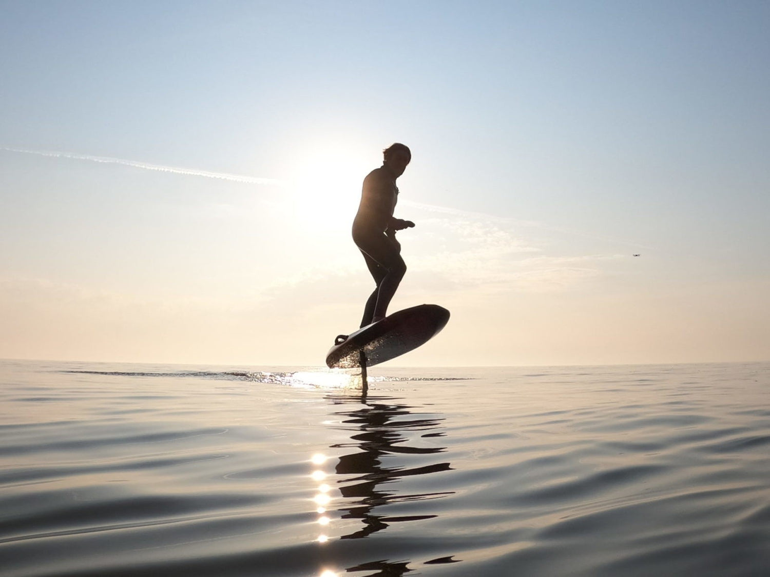 Silhouette van een man op een eFoil op het water met zon in de achtergrond
