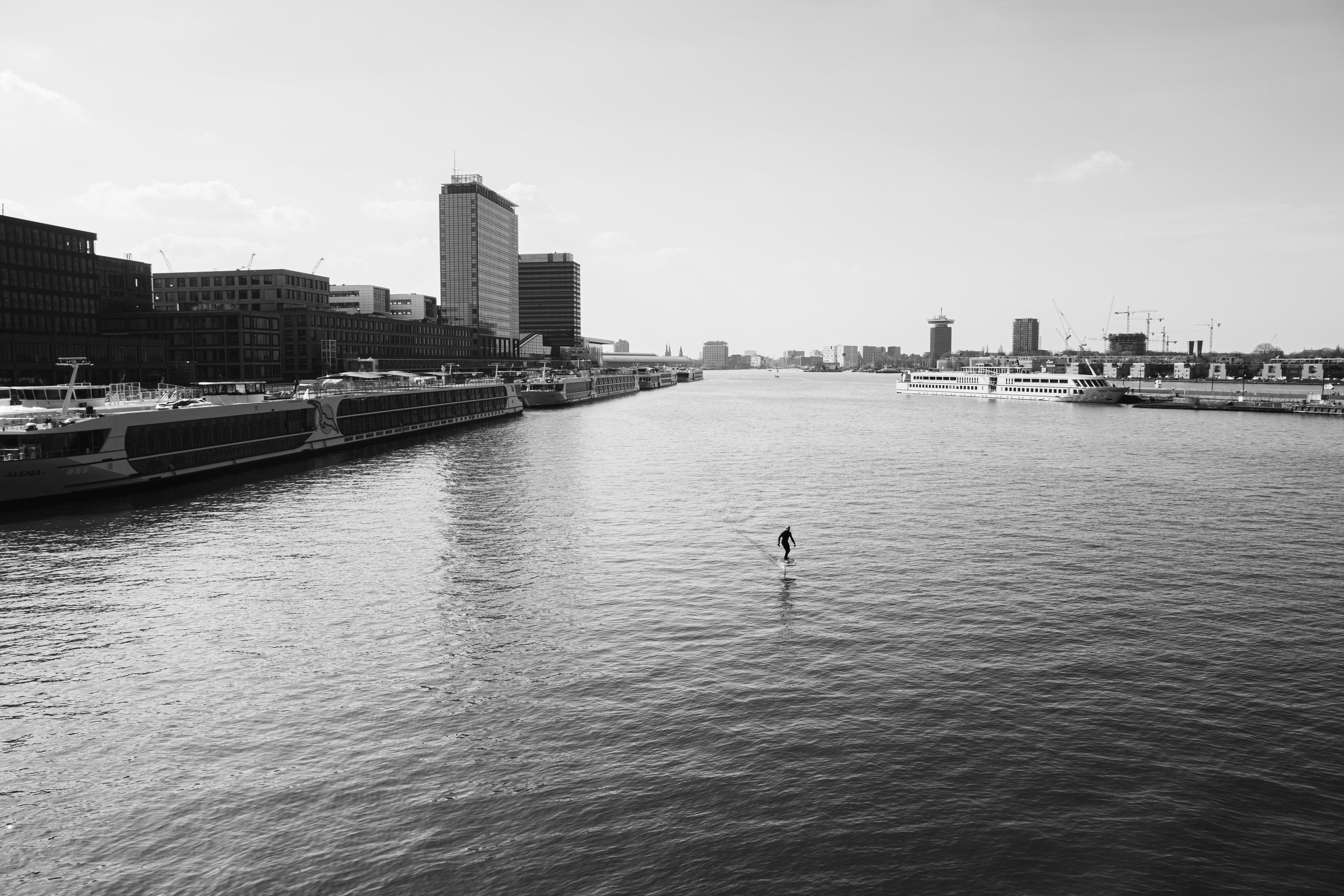 Man surft op een eFoil over het water in Amsterdam met moderne gebouwen en boten op de achtergrond