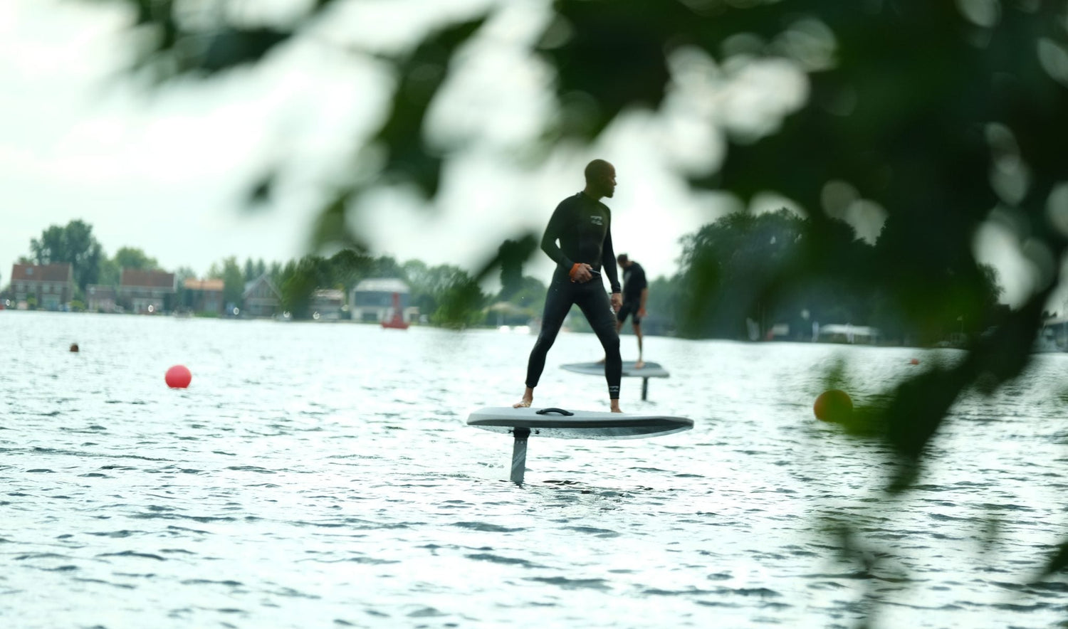 Twee personen aan het eFoilen op het water met groene balderen wazig op de voorgrond