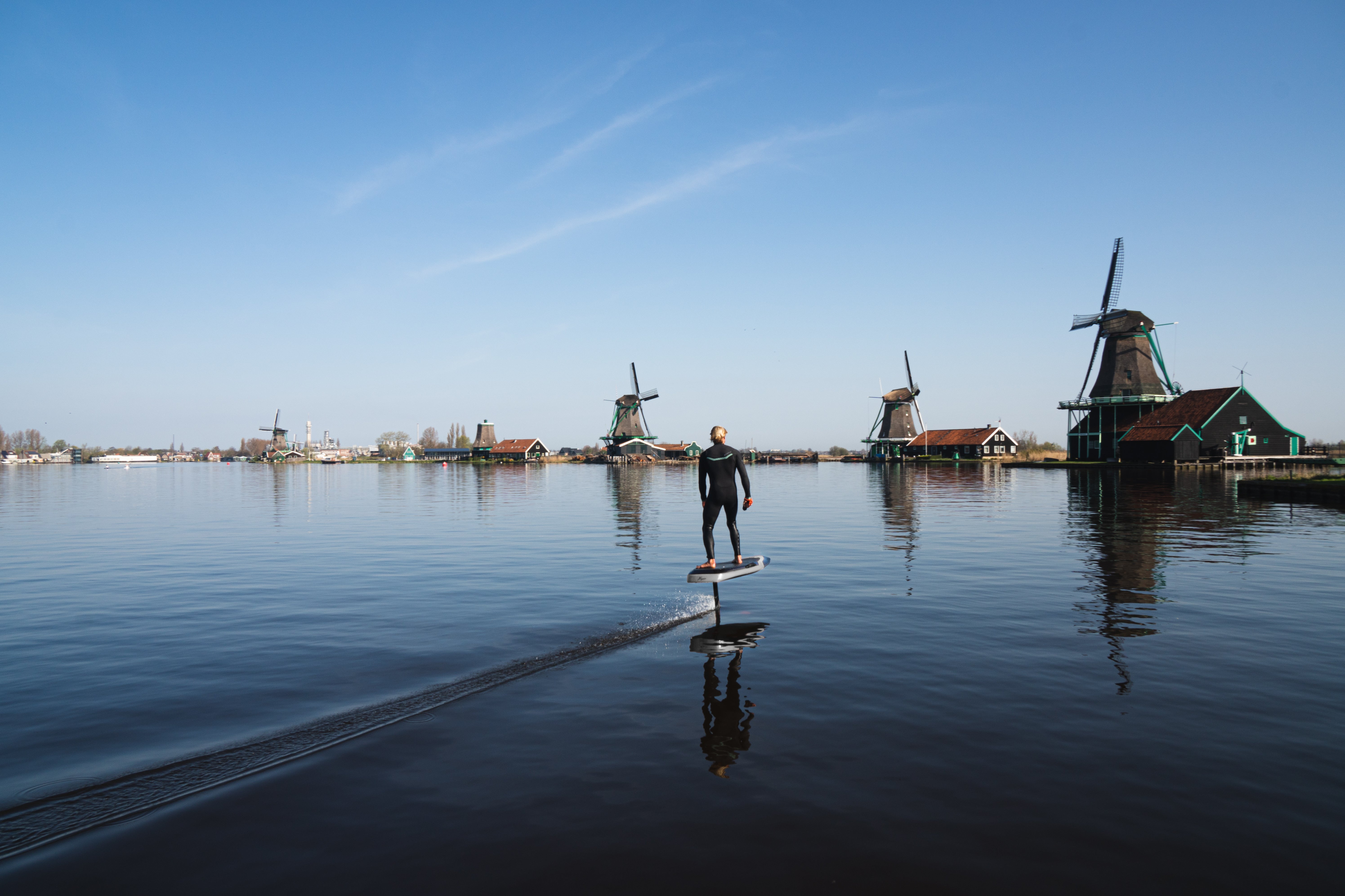 Man in een wetsuit op het water aan het eFoilen bij de Zaanse Schans