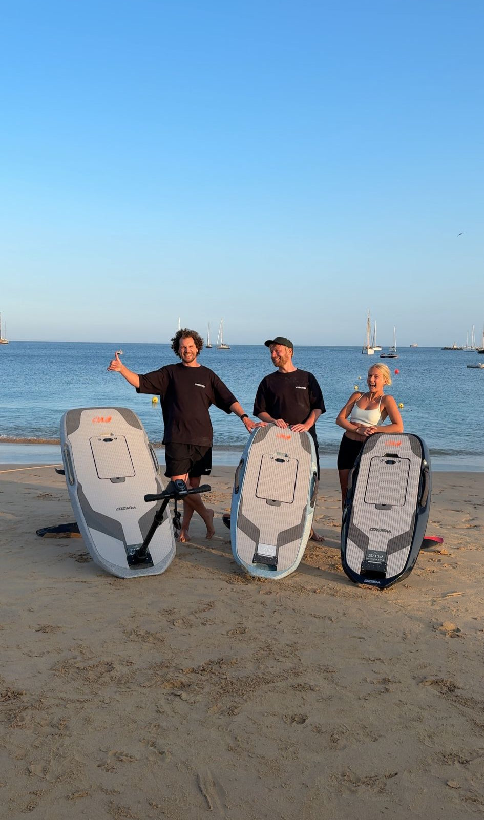 Drie medewerkers van Flying Fish Foils poseren op het strand met allemaal een eFoil
