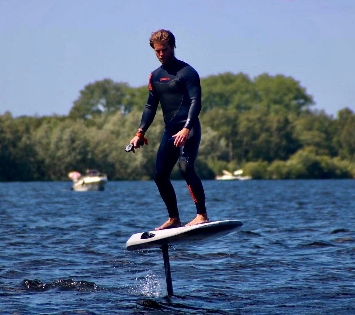 Man in een wetsuit aan het eFoilen op het water met boten op de achtegrond