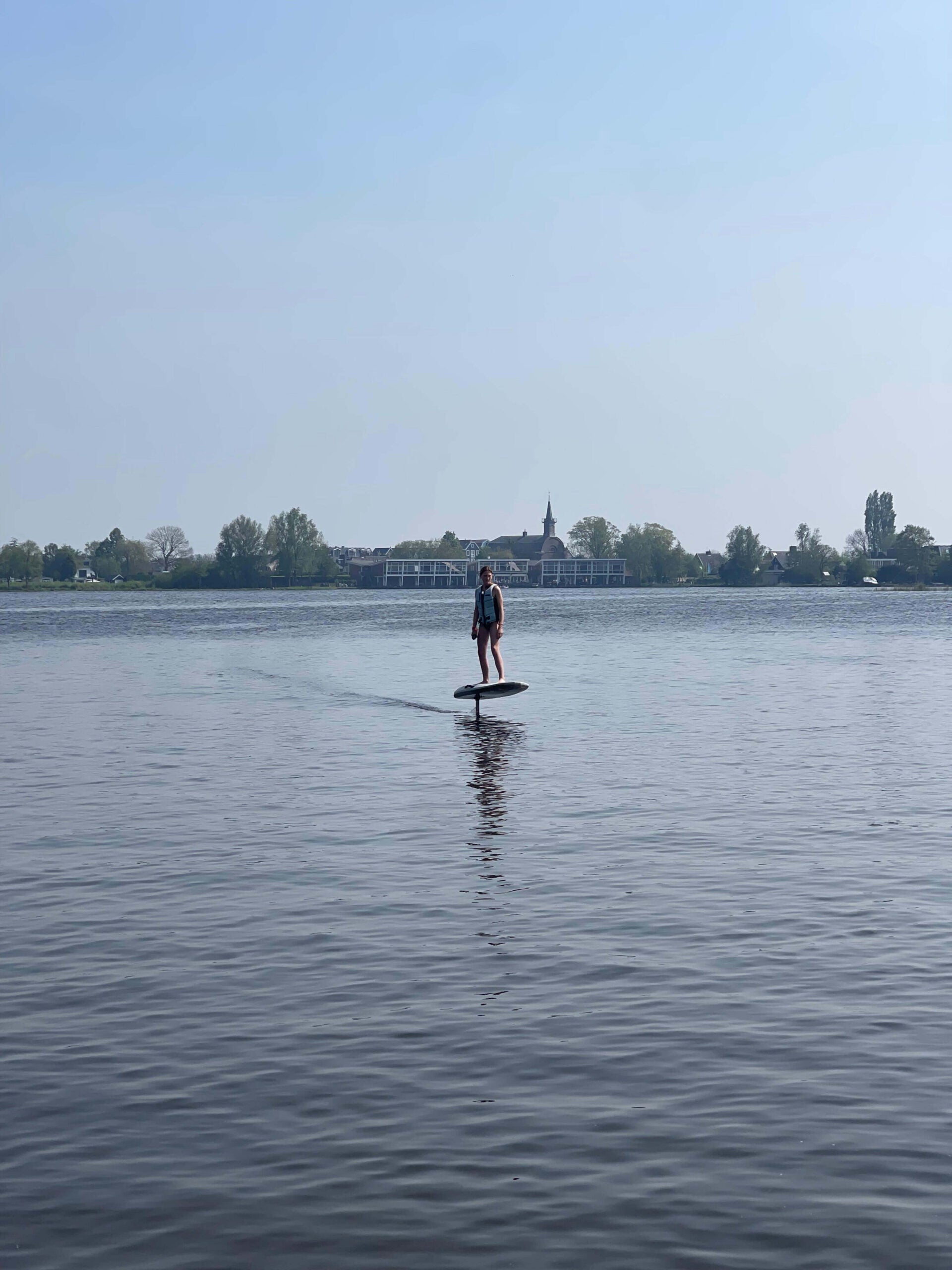 Vrouw aan het eFoilen op het water met bomen, huizen en een kerk in de achtergrond